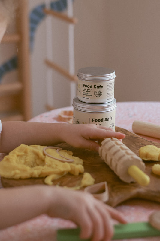 Child playing with play dough on a table with food-safe wax containers in the background.