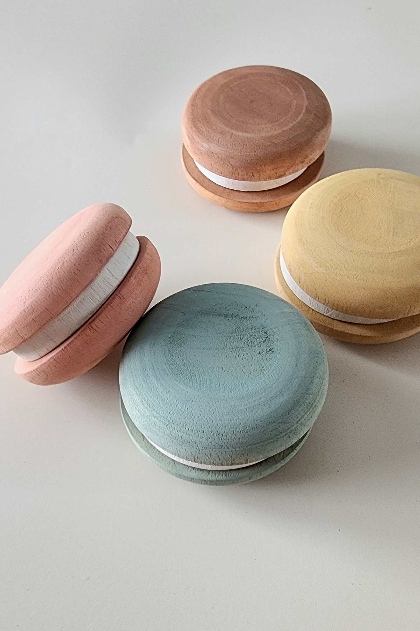 A set of four assorted wooden macarons in pink, brown, blue, and yellow colors, designed for children's pretend play.